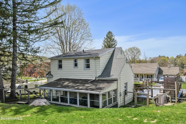 rear view of house featuring a sunroom, roof with shingles, and a lawn