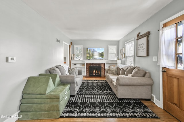 living area featuring plenty of natural light, a brick fireplace, wood finished floors, and visible vents