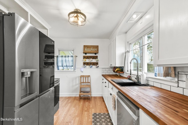 kitchen featuring light wood-style floors, white cabinets, a sink, wood counters, and appliances with stainless steel finishes