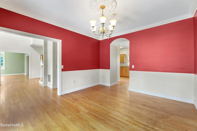 spare room featuring arched walkways, a notable chandelier, visible vents, ornamental molding, and wood finished floors