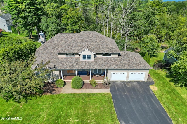 view of front of property featuring a shingled roof, a chimney, aphalt driveway, an attached garage, and a front lawn