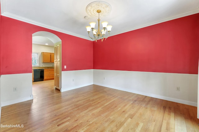 spare room featuring light wood finished floors, arched walkways, a notable chandelier, and ornamental molding