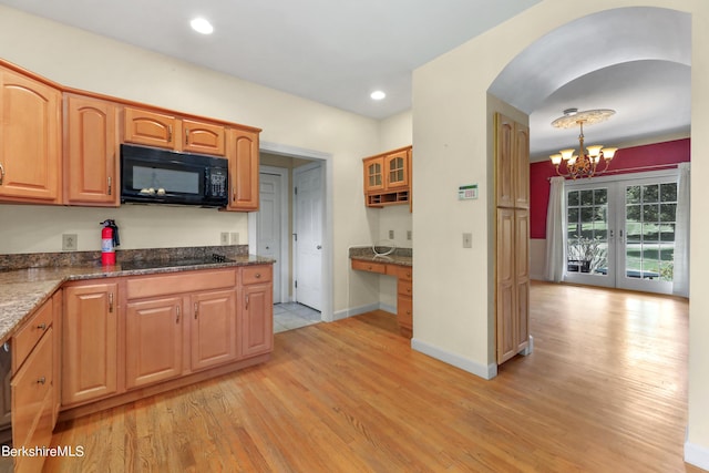 kitchen with hanging light fixtures, light wood-type flooring, black appliances, dark stone countertops, and glass insert cabinets