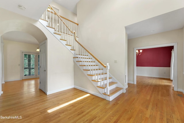 stairway featuring arched walkways, wood finished floors, and baseboards