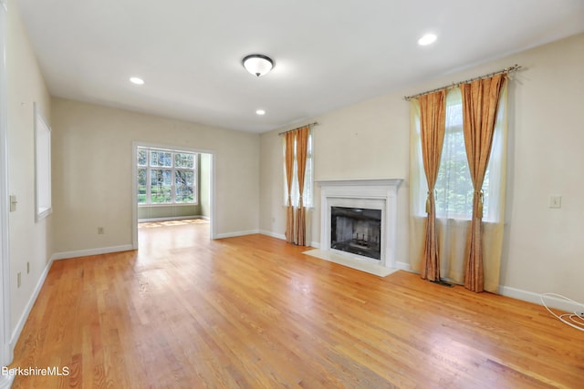 unfurnished living room with baseboards, a fireplace with flush hearth, and light wood-style floors