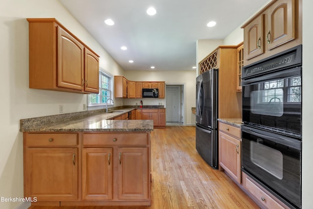 kitchen with kitchen peninsula, dark stone counters, sink, black appliances, and light hardwood / wood-style floors