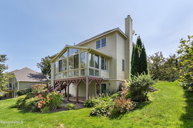 back of property featuring a chimney, a sunroom, a yard, and stairway