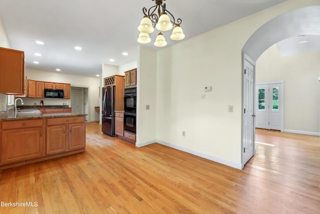 kitchen featuring arched walkways, brown cabinets, hanging light fixtures, a sink, and black appliances