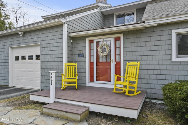 view of exterior entry with a chimney, a shingled roof, and a garage