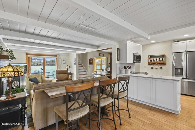 kitchen featuring a peninsula, light wood finished floors, stainless steel appliances, beam ceiling, and open floor plan