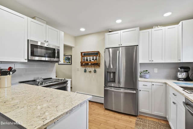 kitchen featuring decorative backsplash, white cabinets, light wood finished floors, a baseboard radiator, and stainless steel appliances
