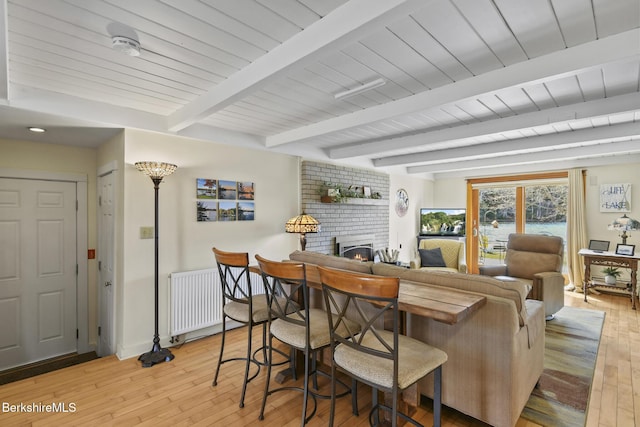 dining area featuring wooden ceiling, beam ceiling, a brick fireplace, baseboards, and light wood-style floors