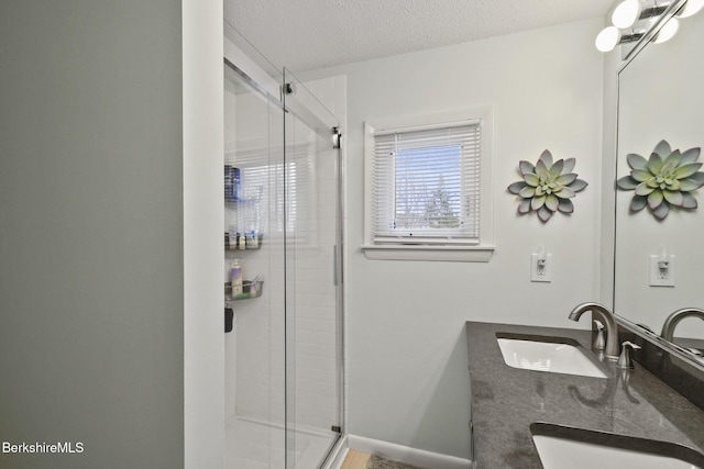 bathroom with double vanity, a sink, a stall shower, and a textured ceiling
