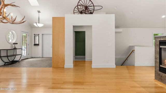 2017 Monterey Rd, Otis, MA 01253 - unfurnished living room featuring a wall mounted air conditioner, light wood-style flooring, lofted ceiling, a skylight, and a tile fireplace