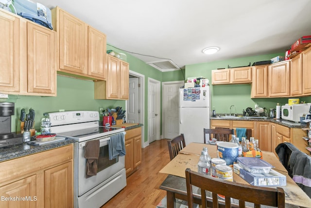 kitchen featuring light brown cabinets, dark countertops, white appliances, light wood-style floors, and a sink