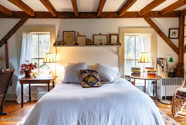 bedroom featuring beam ceiling, radiator, wood-type flooring, and multiple windows