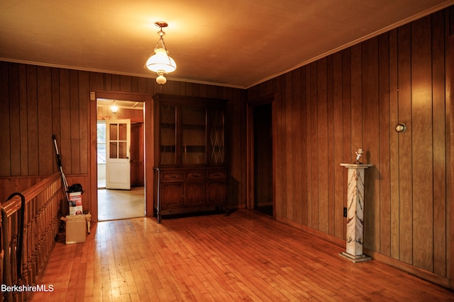 unfurnished room featuring wood walls, ornamental molding, and light wood finished floors
