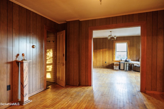 empty room with wood-type flooring, wooden walls, a notable chandelier, and ornamental molding