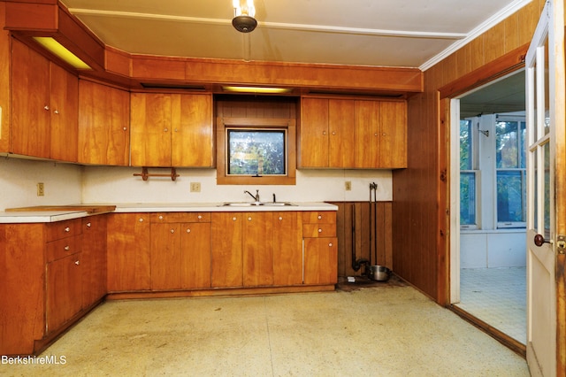 kitchen with light countertops, ornamental molding, brown cabinetry, and a sink