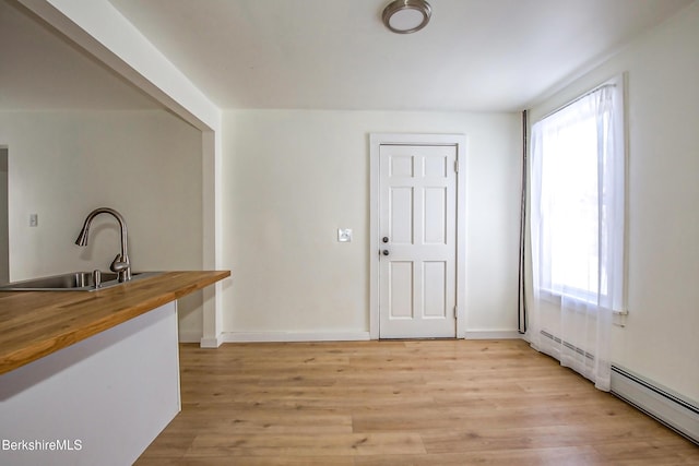 kitchen with butcher block countertops, light hardwood / wood-style flooring, a baseboard heating unit, and sink