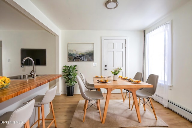 dining room with sink, a baseboard radiator, and light wood-type flooring