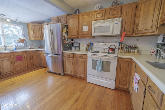 kitchen with light wood-type flooring, tasteful backsplash, a textured ceiling, white appliances, and sink