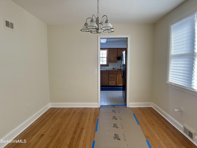 unfurnished dining area featuring an inviting chandelier and light hardwood / wood-style flooring