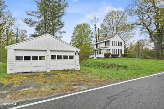 view of front facade with a detached garage, an outbuilding, and a front lawn