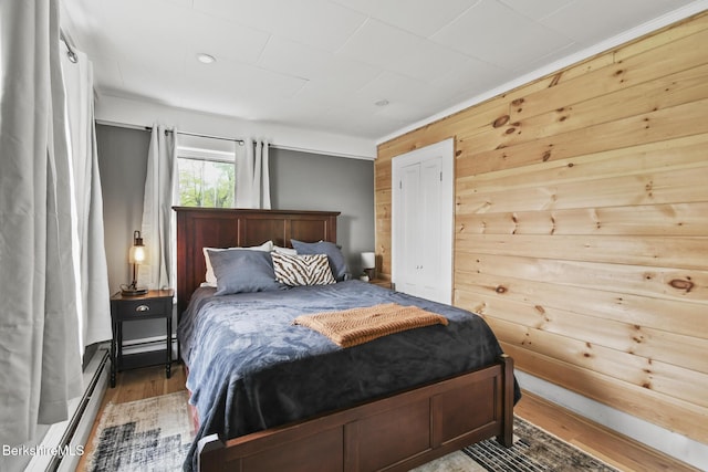bedroom with wood finished floors, a baseboard radiator, and wood walls