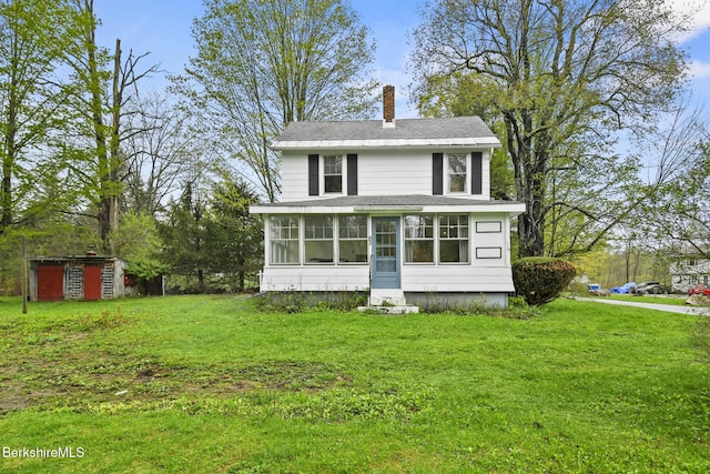 view of front of house featuring a chimney, a sunroom, a front yard, and a shed