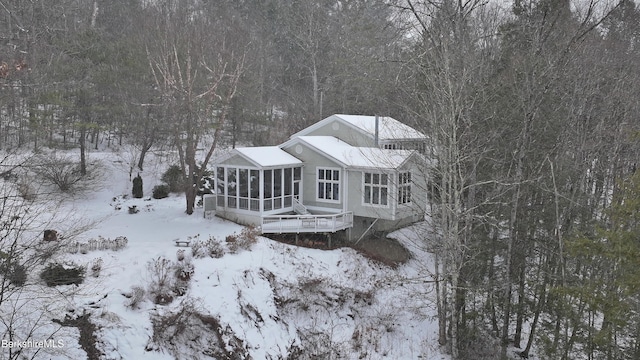 snow covered rear of property with a sunroom