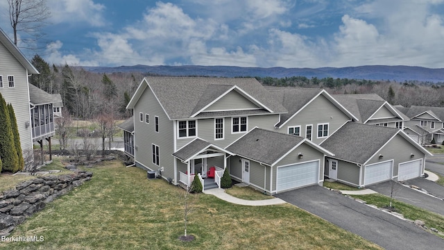 view of front facade with driveway, roof with shingles, a front yard, a mountain view, and a garage