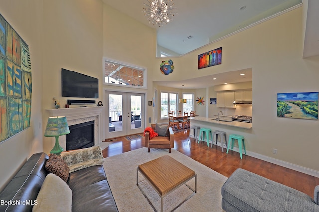 living room featuring wood finished floors, french doors, baseboards, a fireplace, and a notable chandelier