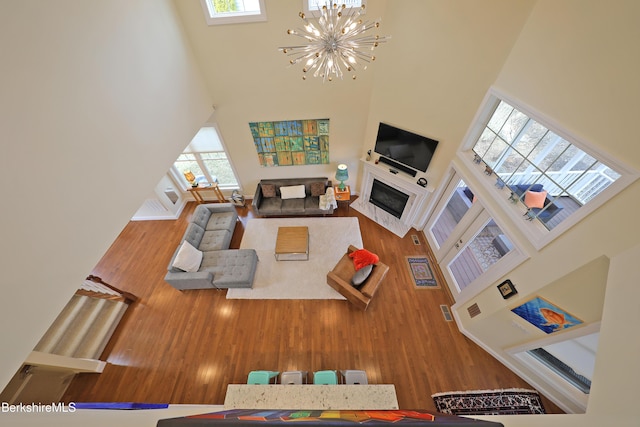 living area with a chandelier, a healthy amount of sunlight, wood finished floors, and a towering ceiling