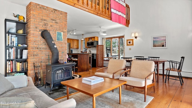 living area with ceiling fan, baseboard heating, a wood stove, and light wood finished floors