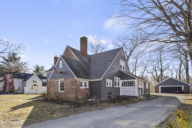 view of side of property featuring an outbuilding, a detached garage, a shingled roof, brick siding, and a chimney