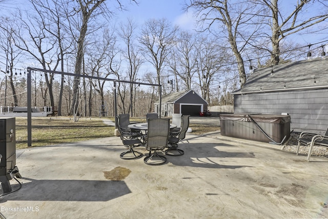 view of patio / terrace with a hot tub, a detached garage, concrete driveway, outdoor dining area, and an outbuilding