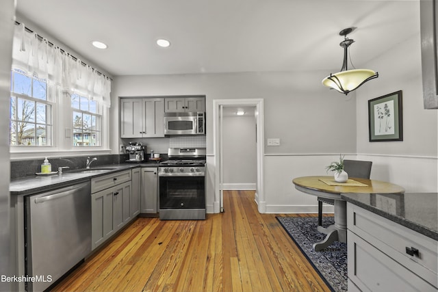 kitchen with gray cabinets, a sink, appliances with stainless steel finishes, decorative light fixtures, and light wood-type flooring