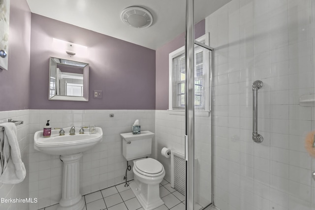 bathroom with tile patterned flooring, toilet, wainscoting, a stall shower, and tile walls