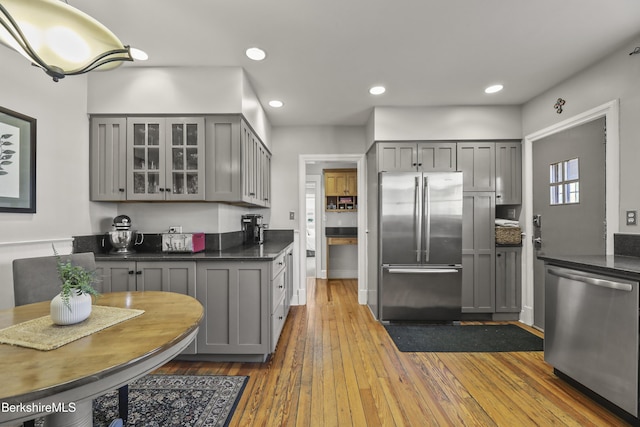 kitchen featuring gray cabinetry, glass insert cabinets, recessed lighting, appliances with stainless steel finishes, and hardwood / wood-style flooring