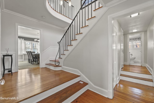 stairway featuring baseboards, wood-type flooring, an inviting chandelier, and crown molding