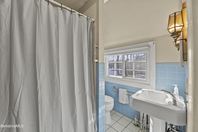 bathroom featuring a sink, wainscoting, tile patterned floors, toilet, and tile walls