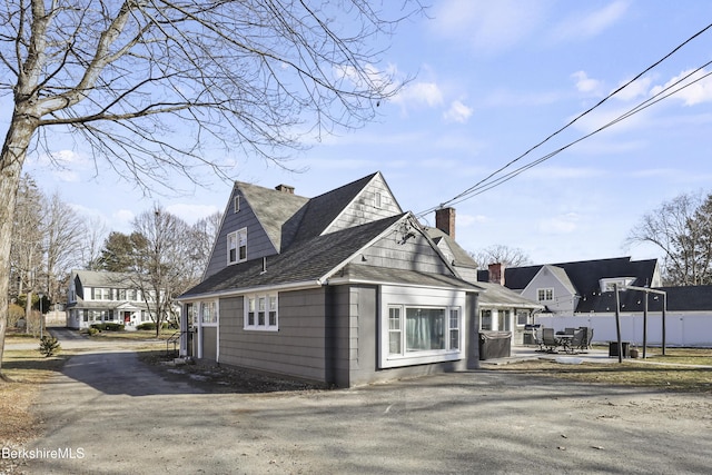 view of side of property featuring a shingled roof, a residential view, a chimney, a patio area, and driveway