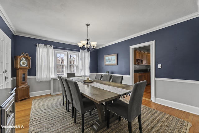 dining room featuring light wood finished floors, a notable chandelier, crown molding, and baseboards