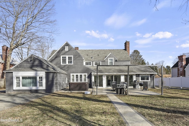 back of property with a hot tub, fence, a yard, a chimney, and a patio area