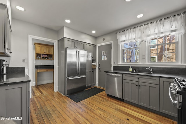 kitchen with gray cabinetry, light wood-type flooring, recessed lighting, appliances with stainless steel finishes, and a sink