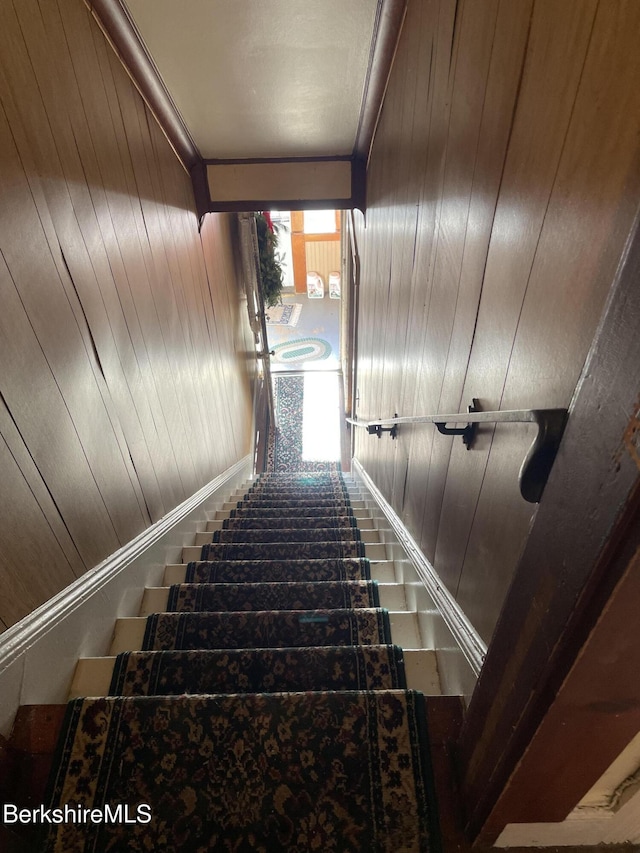 stairs with crown molding and wooden walls