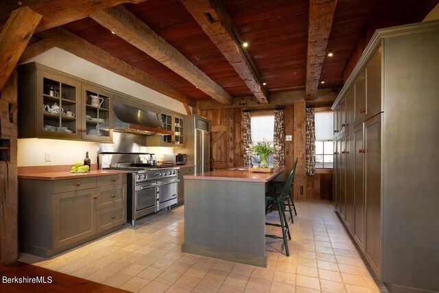 kitchen with butcher block counters, a center island, wall chimney exhaust hood, beamed ceiling, and high end appliances