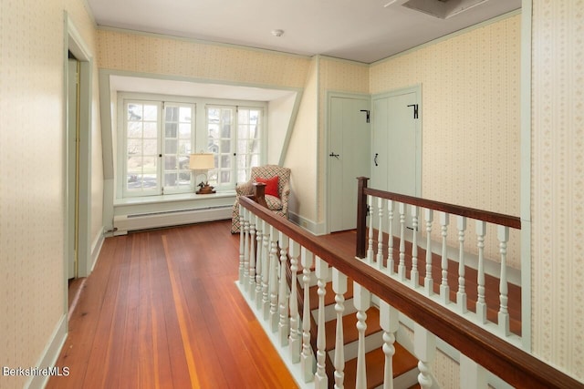 corridor with wood-type flooring, ornamental molding, and a baseboard radiator