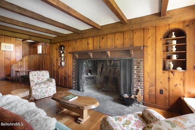 living room featuring hardwood / wood-style flooring, built in shelves, beam ceiling, and a brick fireplace